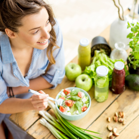 Une femme est en train de manger sainement avec une salade, du jus et des fruits