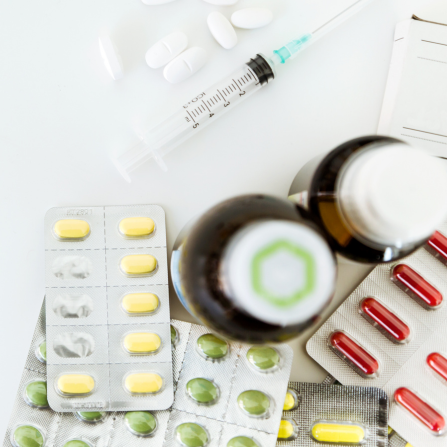 Plusieurs médicaments sont disposés sur un table : sirop, comprimés, gélules, seringue