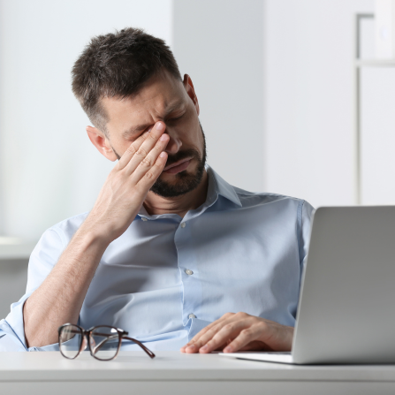 Un homme a mal à la tête devant son ordinateur et pose une main devant ses yeux