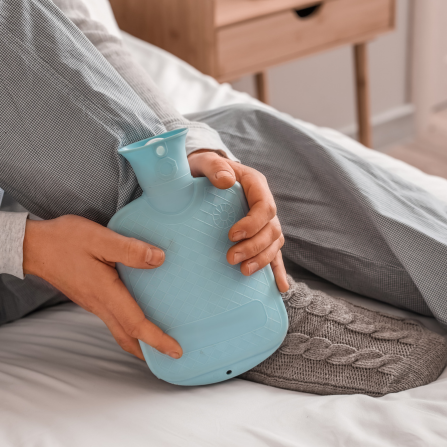 une femme tient dans ses mains une bouillotte et la pose près de ses pieds