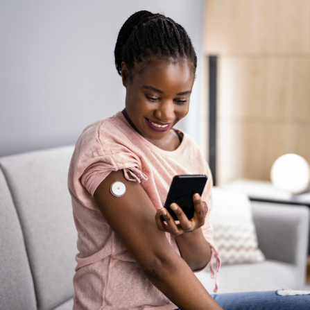 Une femme utilise son téléphone et son capteur de glucose pour mesure sa glycémie