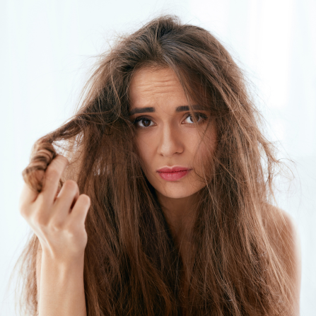 Une femme aux cheveux très secs tient une mèche de ses cheveux entre ses doigts