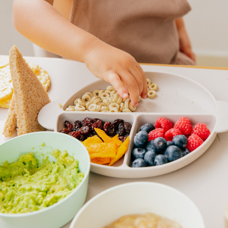 Une enfant mange dans son assiette remplie de céréales, fruits et légumes