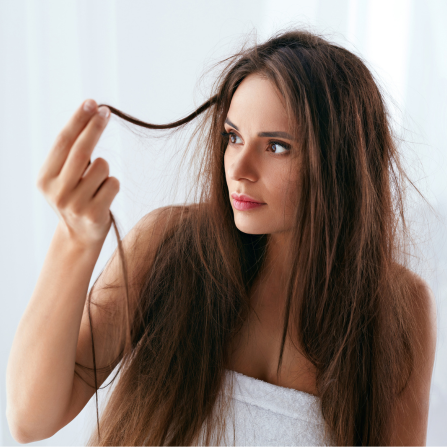 Une femme tient une mèche de ses cheveux abîmés entre ses doigts et la fixe pour en analyser l'état