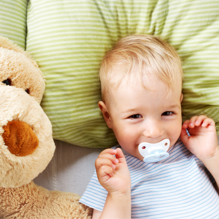 Un enfant avec une tétine est allongé près de son doudou