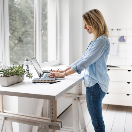 Une femme se tient debout dans sa cuisine et travaille sur son ordinateur portable posé sur son plan de travail