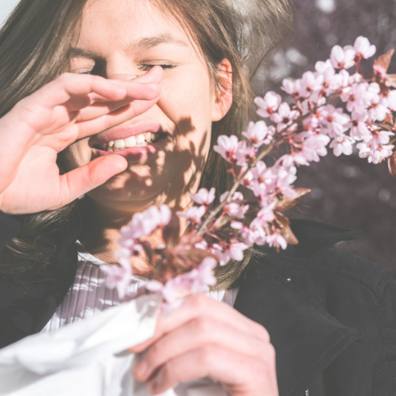 Une femme éternue face à une branche d'arbre remplie de fleurs