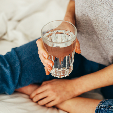 une femme tient un verre d'eau assise dans son lit