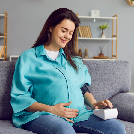 Une femme enceinte mesure sa tension assise dans son canapé