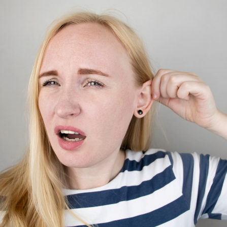 Une femme se tient l'oreille car elle entend mal
