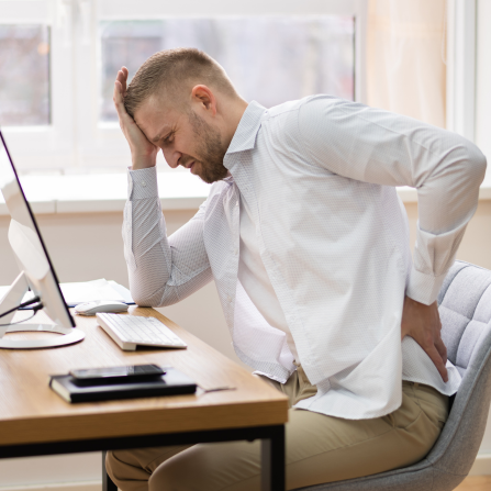Un homme courbé à son bureau devant son ordinateur se tient la tête et le bas du dos en grimaçant
