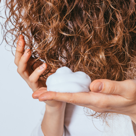 Une femme aux cheveux bouclés s'applique un soin capillaire