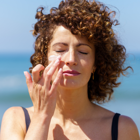 Une femme à la page, présentant des taches pigmentaires, s'applique de la crème solaire sur le visage