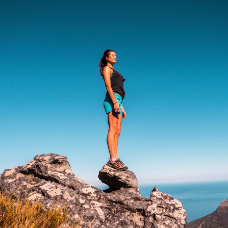 Une femme se tient droite sur un rocher en haut d'une montagne et respire à pleins poumons
