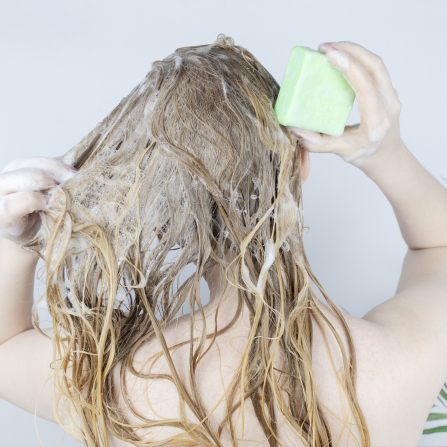 Une femme se lave les cheveux avec un shampoing solide