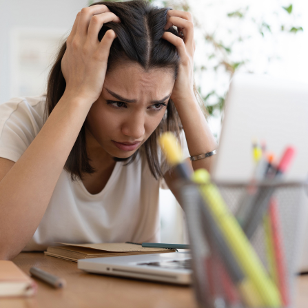 Une femme stress pour ses examens, elle se tient la tête face à son ordinateur portable