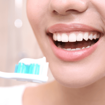 Une femme qui sourit tient une brosse à dents avec du dentifrice
