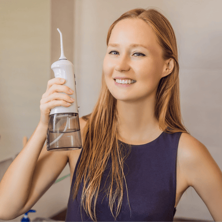 Une femme heureuse tient un jet dentaire portable dans sa main droite